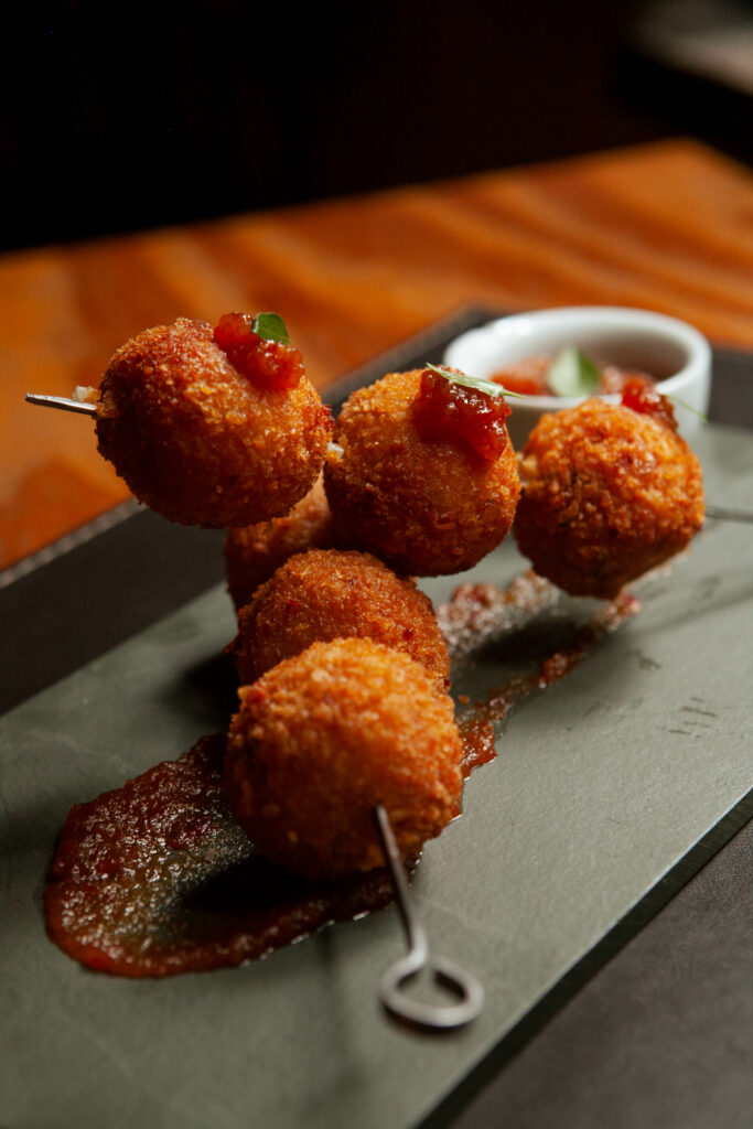 Foto prato Arancini de linguíça blumenau:
Bolinhos fritos de risoto, recheados com linguiça blumenau. Acompanha geléia de pimenta da casa.